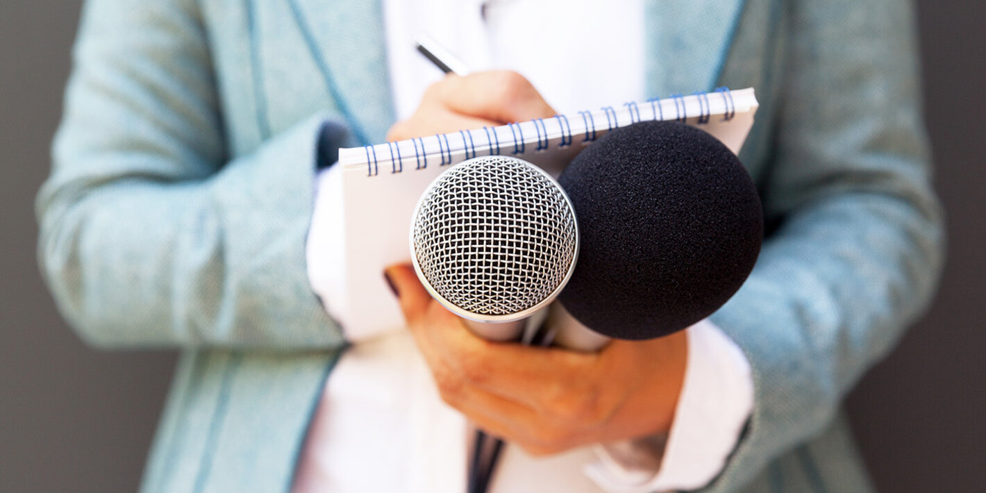 Female reporter at press conference, writing notes, holding microphone